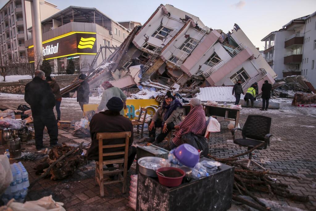 People sit and stand around a collapsed buildings in Golbasi, in Adiyaman province, southern Turkey, 8 February 2023.