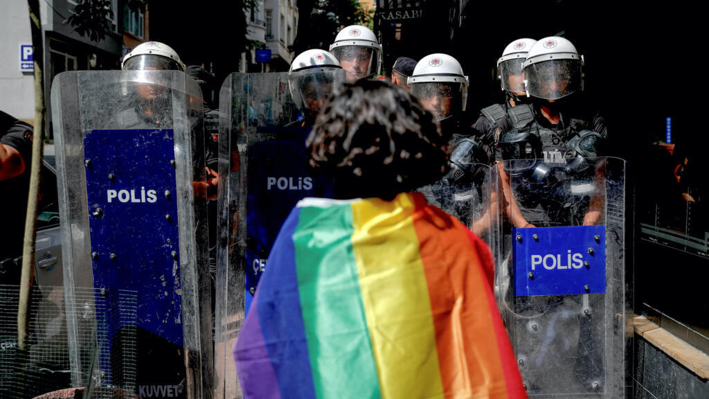 A participant faces riot policemen wearing a rainbow flag during a Pride march in Istanbul, on June 26, 2022.
