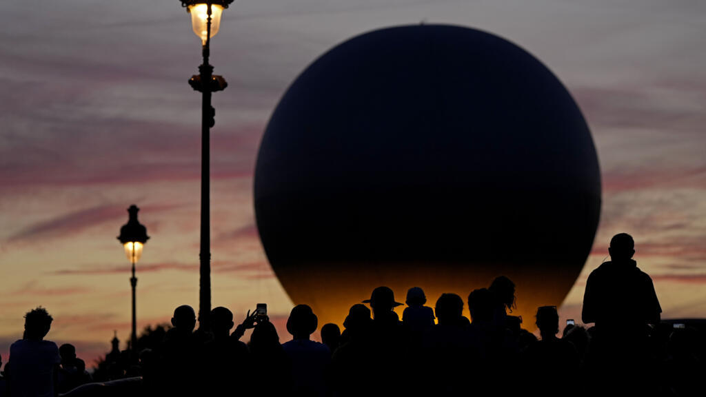 Des personnes attendent que le ballon transportant la vasque olympique s'élève au-dessus du jardin des Tuileries pendant les Jeux olympiques d'été de 2024, mardi 6 août 2024, à Paris, France.