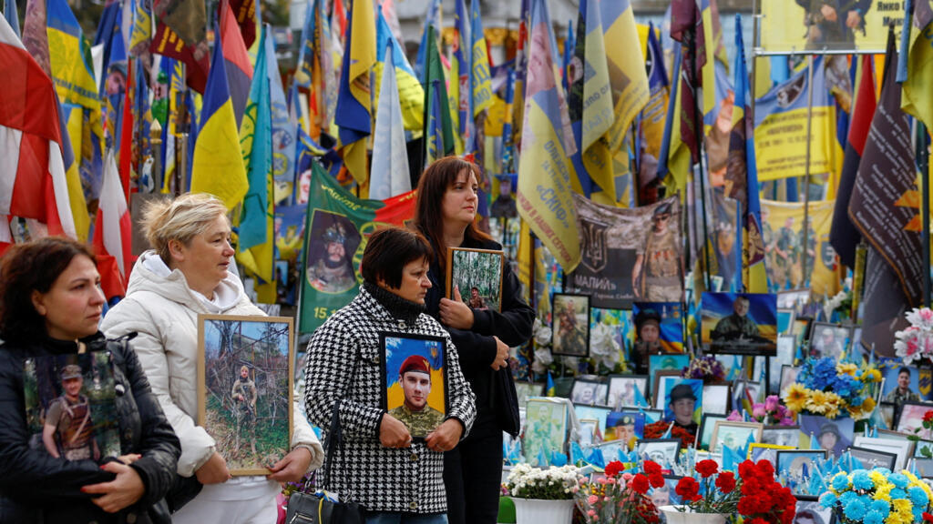 Women carrying portraits of their relatives killed during Russia's attack on Ukraine walk past a makeshift memorial, while Ukrainians mark The Day of Defenders of Ukraine, at the Independence Square in Kyiv, Ukraine October 1, 2025.
