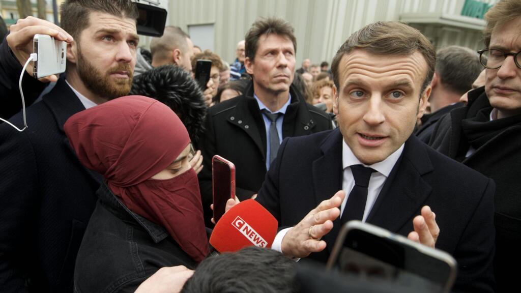 Le président français Emmanuel Macron, entouré de personnes, répond aux questions des journalistes en arrivant au commissariat de police du quartier Bourtzwiller, à Mulhouse, dans l'est de la France, le 18 février 2020