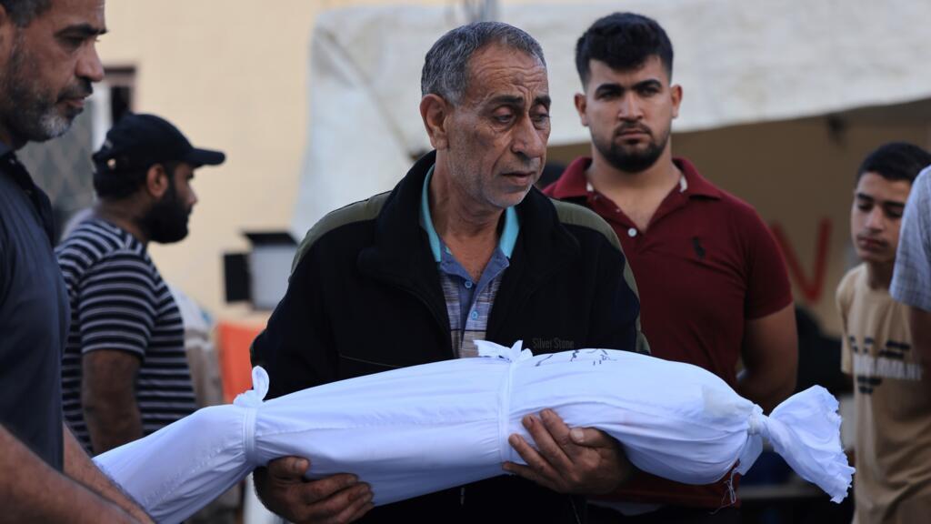Um homem palestino carrega o corpo de uma criança envolta em uma mortalha ao deixar o hospital Shuhada Al-Aqsa, no centro da Faixa de Gaza, em 6 de novembro de 2023.
