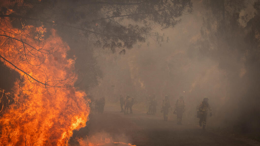 Bombeiros da BRICA (Brigada Especial de Reforço para Incêndios Florestais na Andaluzia) de Granada atravessam as chamas na área de incêndio em direção a uma superfície já queimada durante as operações para combater um incêndio florestal na aldeia de Larouco, na região de Lugo, Galiza, Espanha, em 17 de agosto de 2025.