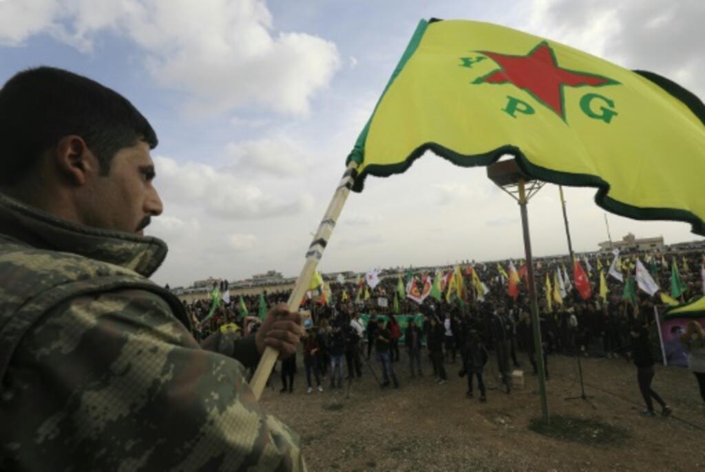 A militant holds the Kurdish People's Protection Units (YPG) flag on a picture taken in the town of Amuda, Syria in 2018.