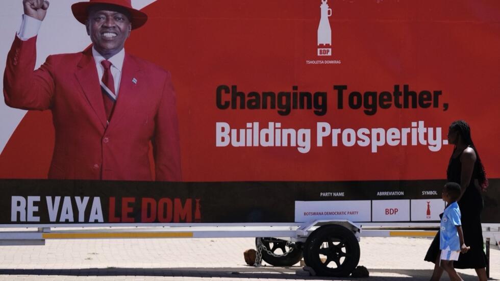 Mwanamke na mtoto wakipita mbele ya bango la uchaguzi la Rais wa Chama cha Kidemokrasia cha Botswana Mokgweetsi Masisi huko Gaborone, Botswana, Jumanne, Oktoba 29, 2024.