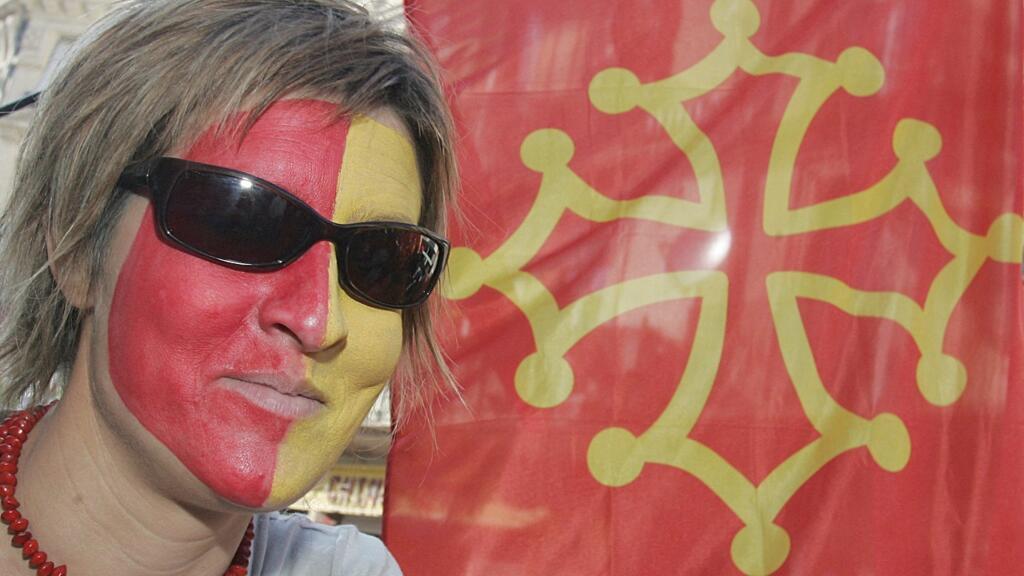 Une femme au visage bariolé aux couleurs de l'Occitanie, à côté d'un drapeau de la région. (illustration)
