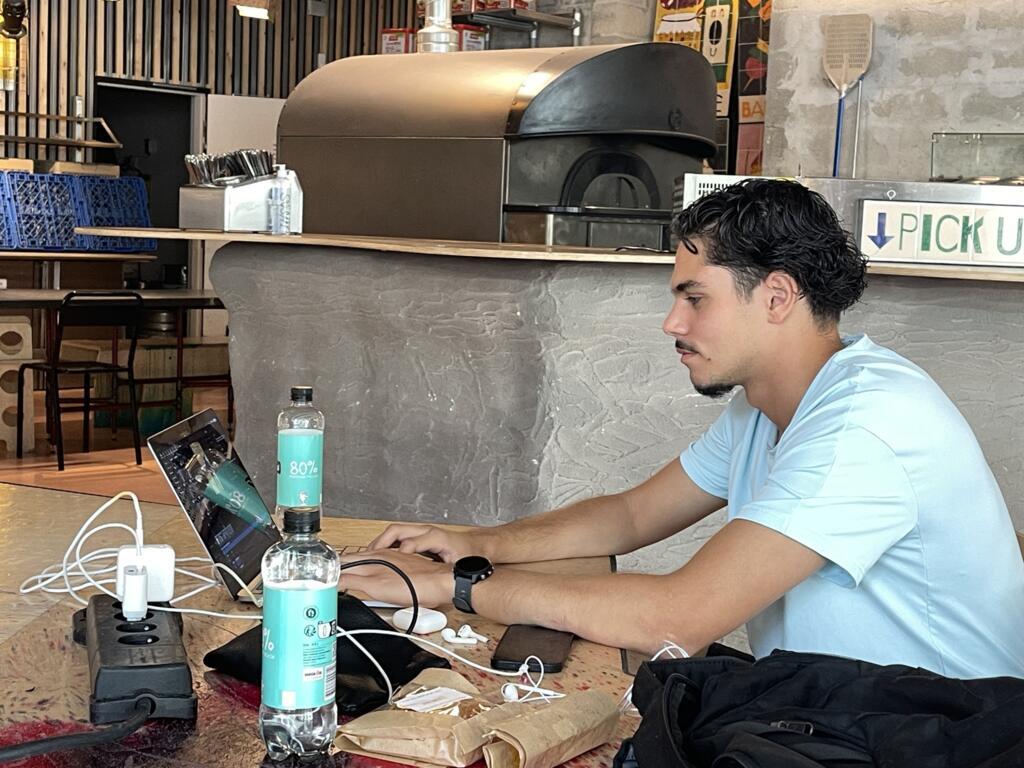 Zakarias Regis trabalha em seu computador na praça de alimentação de um shopping center. Em Paris, em 12 de agosto de 2025.
