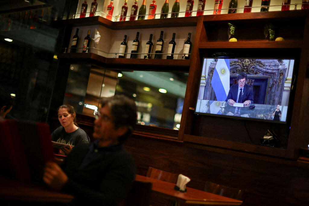 Uma tela mostra o presidente da Argentina, Javier Milei, dirigindo-se às pessoas em rede nacional de TV enquanto as pessoas jantam em um restaurante, em Buenos Aires, Argentina, 22 de abril de 2024.