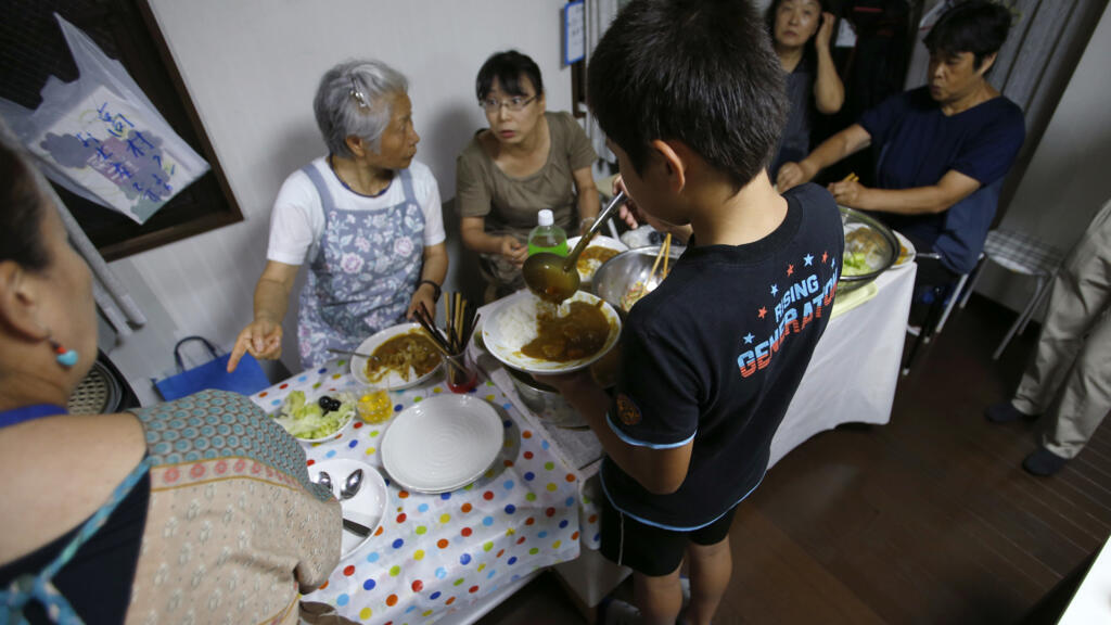 Un garçon verse du curry dans une assiette dans une « cafétéria pour enfants » créée par Misako Omura à Tokyo, le 18 août 2016. Le dîner hebdomadaire d'Omura fait partie du nombre croissant de « kodomo shokudo », ou « cafétérias pour enfants », qui fleurissent à travers le Japon. Les efforts, essentiellement communautaires, visent à résoudre une série de problèmes liés aux enfants, allant de la pauvreté à la garantie que ceux dont les parents travaillent tard aient un bon dîner.