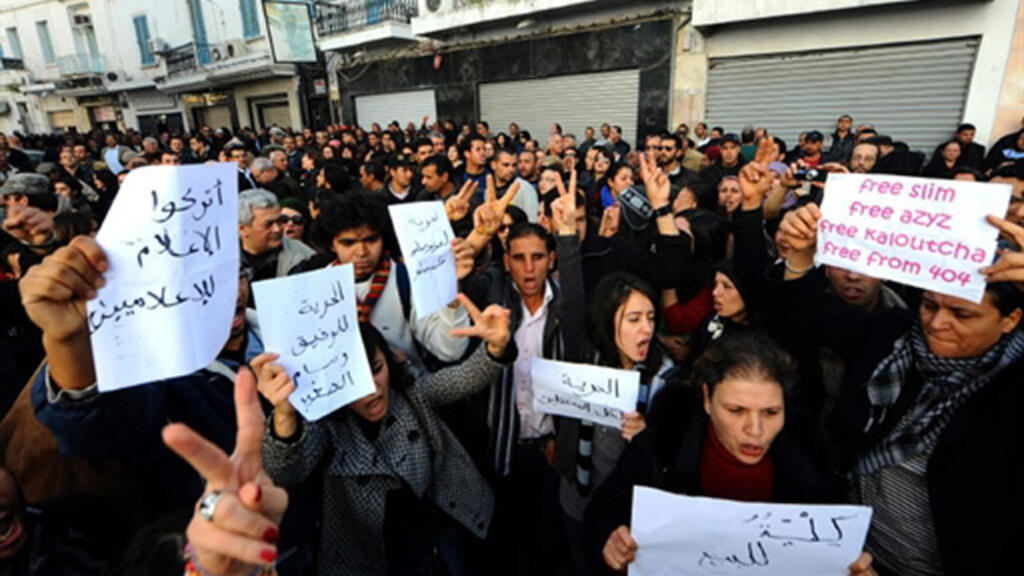 Des manifestants brandissent des affiches et font des signes de victoire pendant un rassemblement à Tunis le 8 janvier 2011, soit six jours avant que Zine el-Abidine Ben Ali n'abandonne le pouvoir.