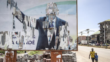 L'ex-président guinéen avait été le premier à être élu démocratiquement dans le pays. Ici, des Guinées passent à côté d'une affiche d'Alpha Condé, à Conakry le 16 septembre 2021, 11 jours après son renversement. (illustration)