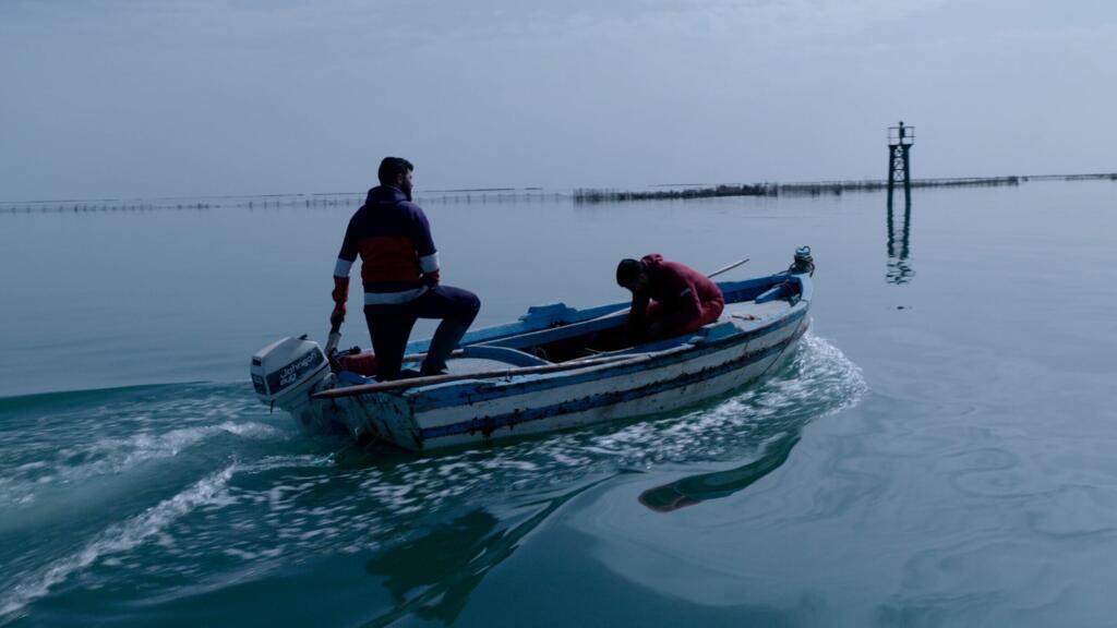Deux pêcheurs partent en mer, avec au loin les charfias, ces pêcheries fixes typiquement kerkéniennes.