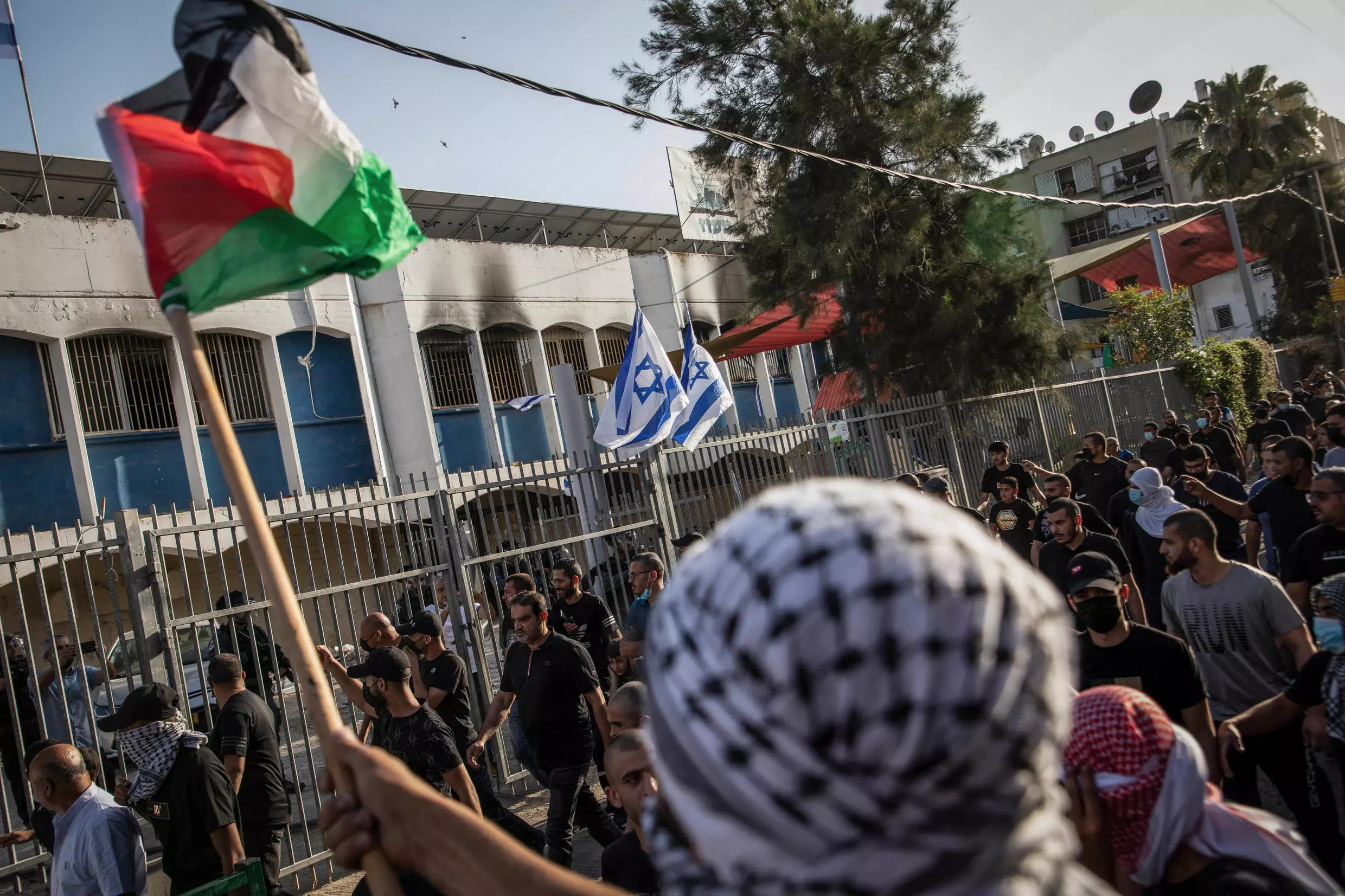 Árabes israelíes gesticulan y ondean banderas palestinas hacia israelíes en un edificio de la comunidad judía, durante los nuevos disturbios en la ciudad de Lod, tras el funeral de un hombre árabe-israelí de 25 años.
