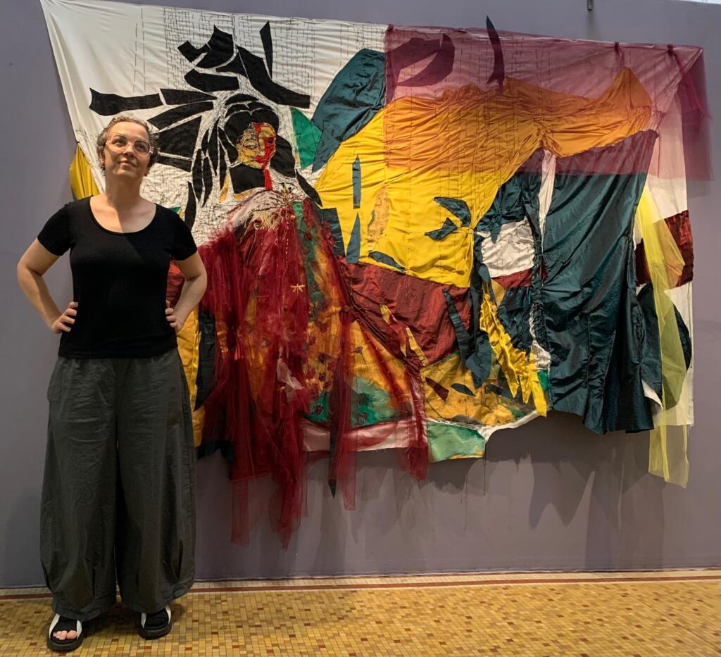 Marcia Tiburi posa em frente a uma das obras presentes na exposição Terradorada, feita inteiramente com tecidos e bordados.