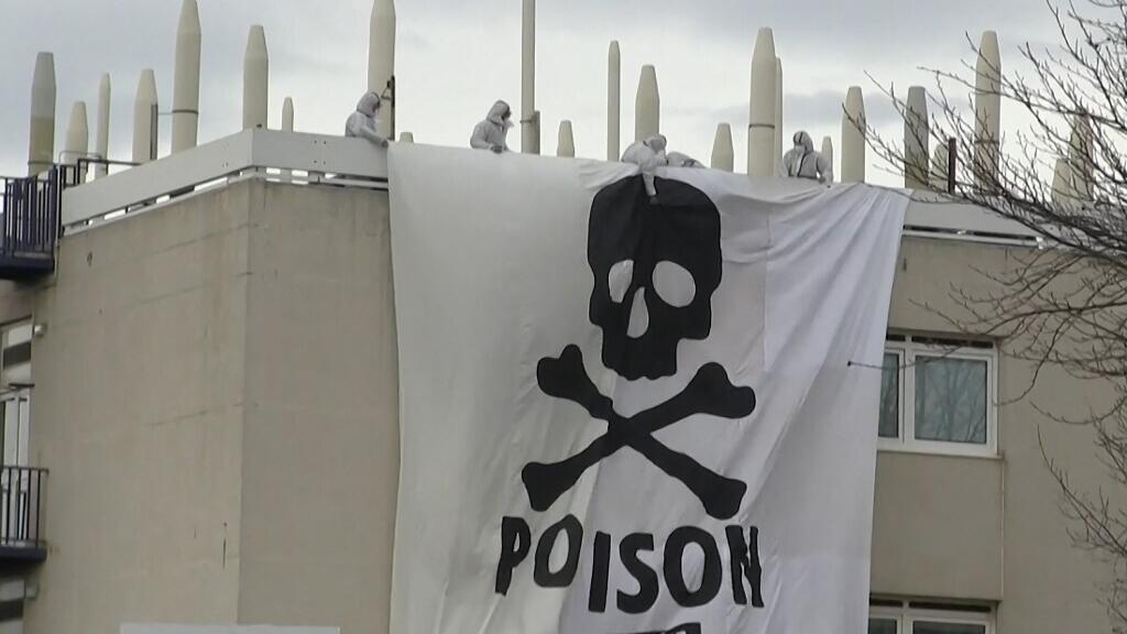 Cette image extraite d'une séquence AFPTV montre des activistes d'Extinction Rebellion et de Youth for Climate déployant une banderole géante représentant un crâne et des os, portant le message "Poison", au sommet d'une structure à l'intérieur de l'usine chimique Arkema après avoir pénétré sur le site pour protester contre la pollution causée par les substances polyfluoroalkyles (PFAS), à Pierre-Bénite, au sud de Lyon, le 2 mars 2024.