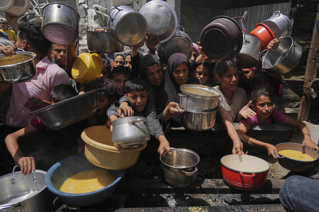 Palestinos tentam receber alimentos doados em uma cozinha, em Jabalia, no norte da Faixa de Gaza, em 19 de maio de 2025.