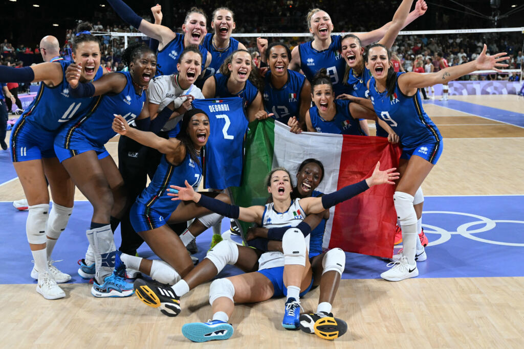Paola sentada no chão na frente da bandeira italiana com suas colegas da seleção da Itália em comemoração, após vencerem a medalha de ouro do vôlei feminino contra os EUA, em Paris 2024, no último dia 11 de agosto.